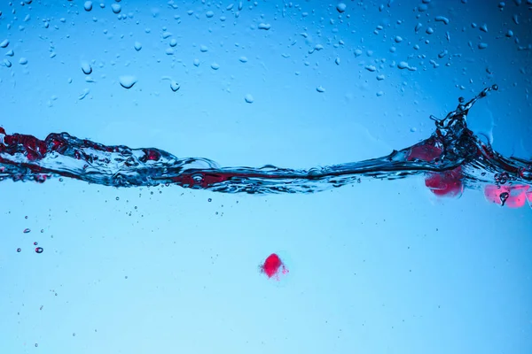 Кубики льоду з ягодами у воді з бульбашками, ізольовані на синьому — стокове фото