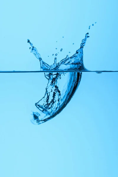 Cubo de hielo en agua con salpicadura, aislado en azul - foto de stock