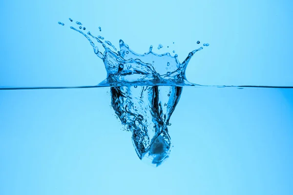 Крижаний куб у прозорій воді з бризкою, ізольований на синьому — стокове фото