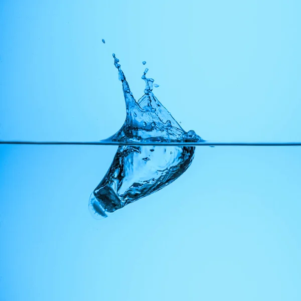 Крижаний куб у прозорій воді, ізольований на синьому — стокове фото