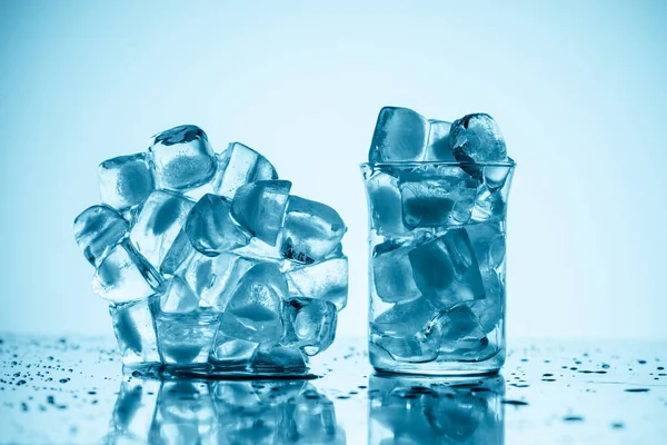 Cubetti di ghiaccio sciolti vicino al vetro e in vetro, su bianco con gocce — Foto stock