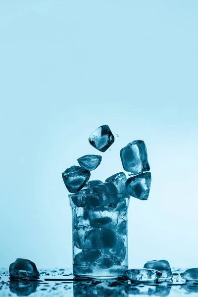 Melting ice cubes falling into glass, on white with drops — Stock Photo