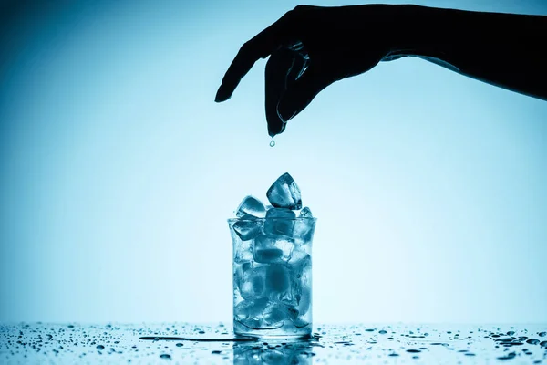 Vista recortada de la persona arrojando cubitos de hielo en el vidrio - foto de stock