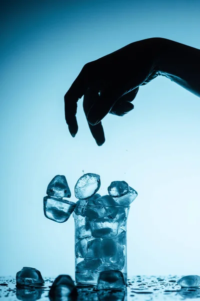Vista recortada de la persona arrojando cubitos de hielo en el vidrio - foto de stock