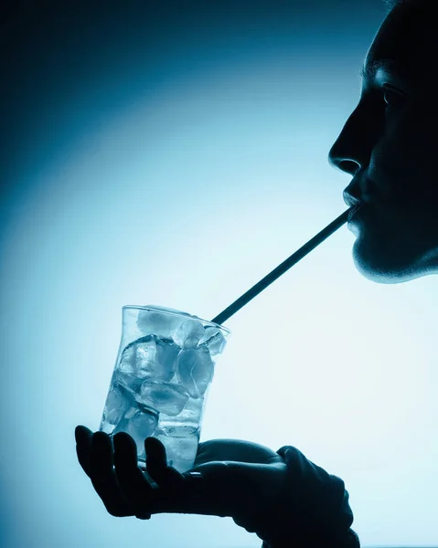 Silhouette of woman drinking cold water with ice cubes with straw — Stock Photo