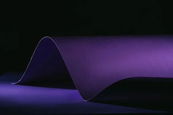 Warping purple paper on purple surface on black — Stock Photo