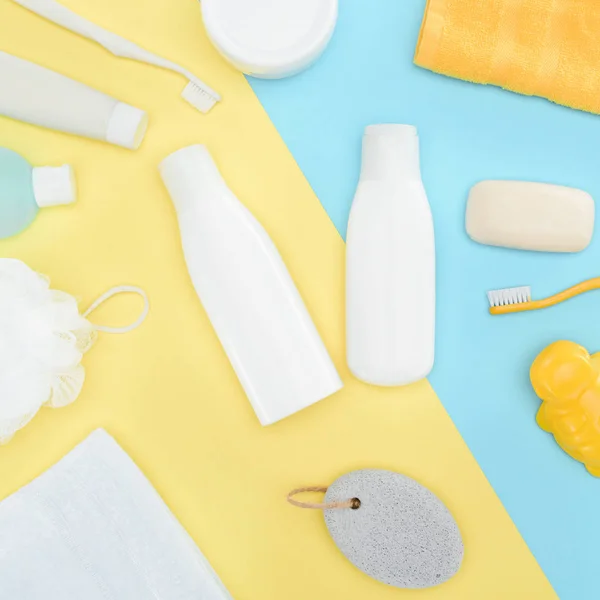 Plat avec lotion pour le corps en bouteilles, brosses à dents, pierre ponce, serviette et savon, isolé sur bleu et jaune — Photo de stock