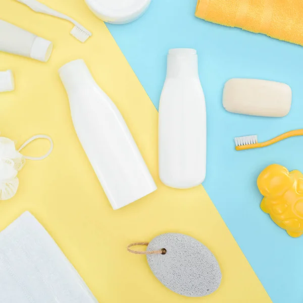 Vista superior de la loción corporal en botellas, cepillos de dientes, pómez, toalla y jabón, aislados en azul y amarillo - foto de stock