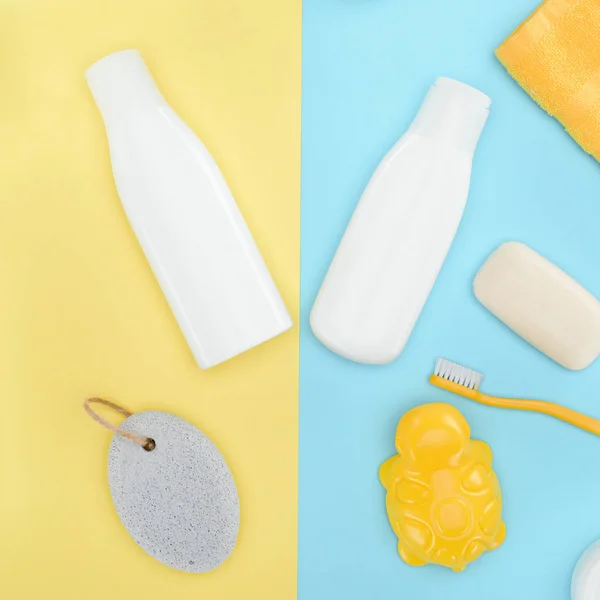 Flat lay com garrafas de loção, escova de dentes, pedra-pomes, sabão e banho brinquedo, isolado em azul e amarelo — Fotografia de Stock