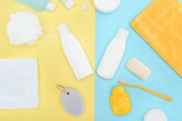 Plat avec lotion pour le corps en bouteilles, brosses à dents, pierre ponce et serviettes, isolé sur bleu et jaune — Photo de stock