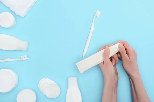 Vista cortada de mulher segurando escova de dentes e pasta de dentes isolada em azul com creme cosmético e garrafas de loção — Fotografia de Stock