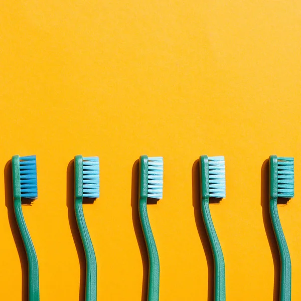 Escovas de dentes verdes em linha, em amarelo com espaço de cópia — Fotografia de Stock