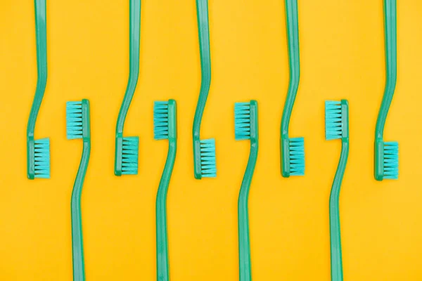 Fondo minimalista con cepillos de dientes verdes en fila, aislados en amarillo - foto de stock