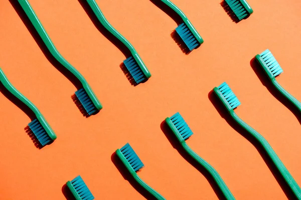 Fondo minimalista con cepillos de dientes verdes, en naranja - foto de stock