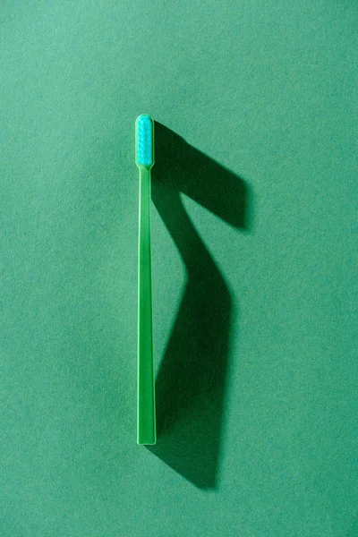 Вид сверху на одну зеленую зубную щетку с тенью, на зеленый — стоковое фото