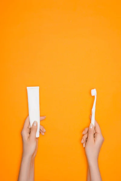 Vista recortada de la mujer sosteniendo cepillo de dientes y tubo de pasta de dientes, aislado en naranja - foto de stock