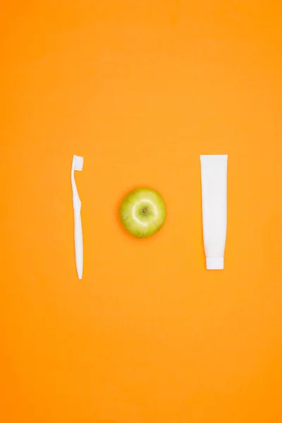 Vista superior del cepillo de dientes, manzana y tubo de pasta de dientes, aislado en naranja - foto de stock