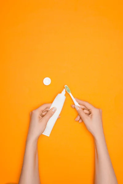 Vista cortada de mulher com escova de dentes e tubo de pasta de dentes, isolado em laranja — Fotografia de Stock