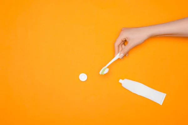 Vista cortada da mulher segurando escova de dentes e tubo de pasta de dentes, isolado em laranja — Fotografia de Stock