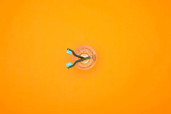Вид сверху на две зубные щетки в чашке, изолированные на оранжевый — стоковое фото