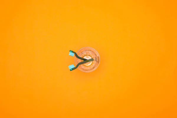 Top view of two toothbrushes in cup, isolated on orange — Stock Photo