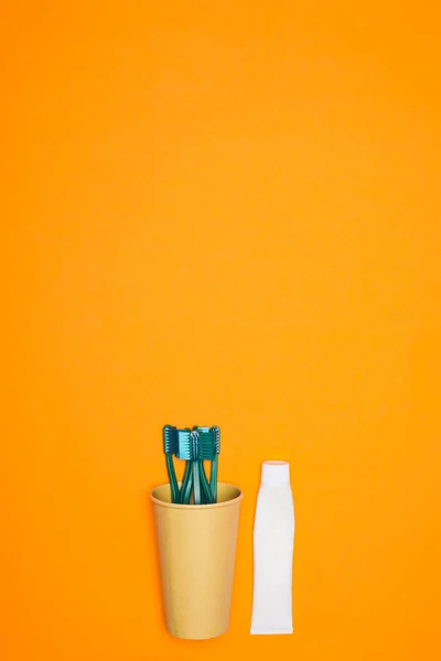 Vista superior de cepillos de dientes en taza de papel y tubo de pasta de dientes, aislado en naranja - foto de stock