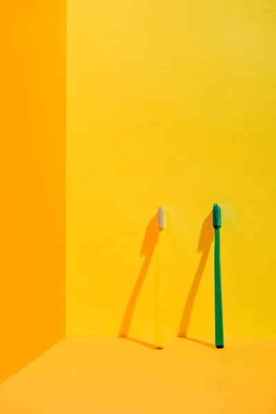 Cepillos de dientes verdes y amarillos en la pared naranja - foto de stock