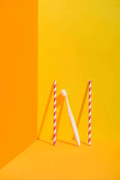Strohhalme und weiße Zahnbürste stehen an oranger Wand — Stockfoto