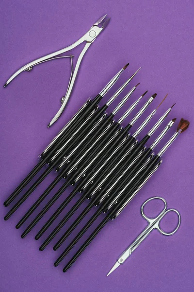 Vista superior de pinças de unhas, escovas e tesouras isoladas em roxo — Fotografia de Stock