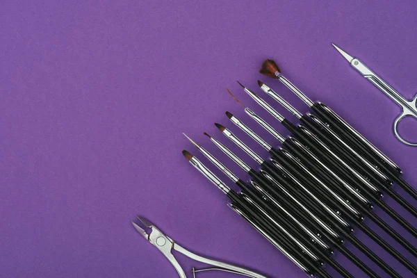 Vista superior de escovas, tesouras e pinças de unhas isoladas em roxo — Fotografia de Stock