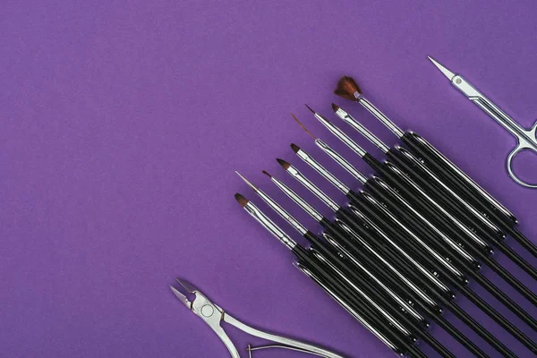 Vue de dessus des pinceaux, ciseaux et pinces à ongles isolés sur violet — Photo de stock