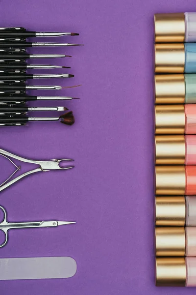 Vista superior de herramientas de manicura y esmaltes de uñas aislados en púrpura - foto de stock