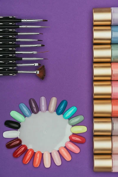 Vue de dessus des vernis à ongles, pinceaux et palette isolés sur violet — Photo de stock