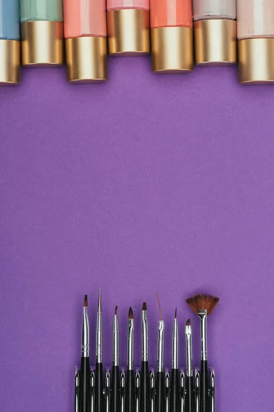 Vue de dessus des vernis à ongles et des brosses isolés sur violet — Photo de stock