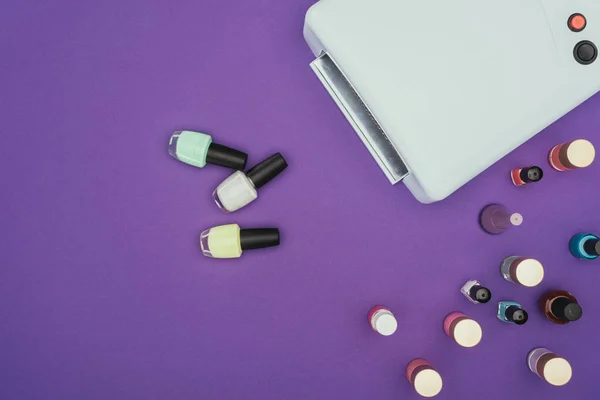 Top view of different nail polishes and uv lamp isolated on purple — Stock Photo