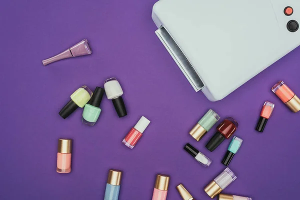 Top view of scattered nail polishes and uv lamp isolated on purple — Stock Photo