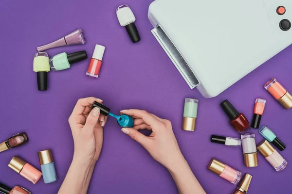 Cropped image of woman holding turquoise nail polish isolated on purple — Stock Photo