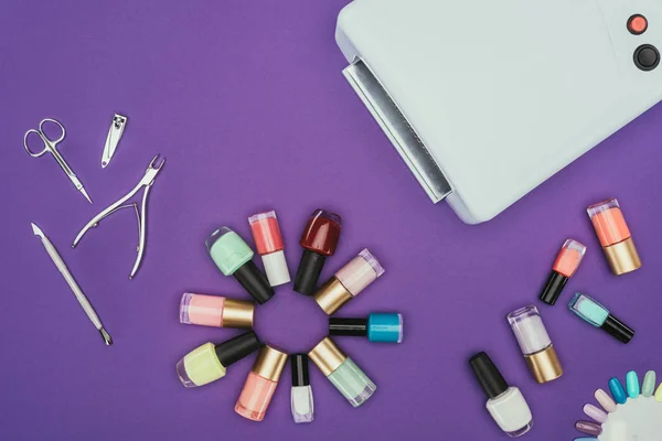 Top view of uv lamp and nail varnishes isolated on purple — Stock Photo