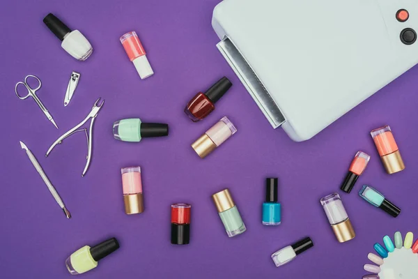 Top view of nails polishes and uv lamp isolated on purple — Stock Photo