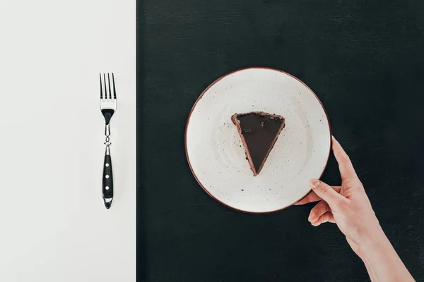 Vista dall'alto della donna in possesso di piatto con pezzo di torta su sfondo nero — Foto stock