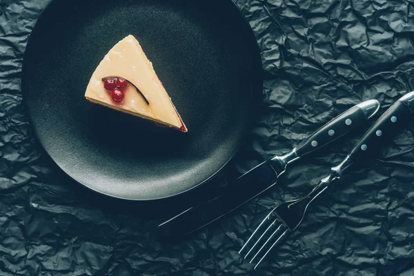 Vue du dessus du morceau de gâteau sur une assiette et des couverts sur une table sombre — Photo de stock