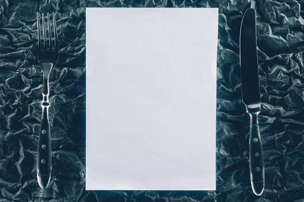 Vista superior de papel en blanco y cubiertos en la mesa oscura - foto de stock