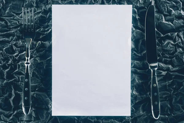 Top view of blank paper and cutlery on dark tabletop — Stock Photo