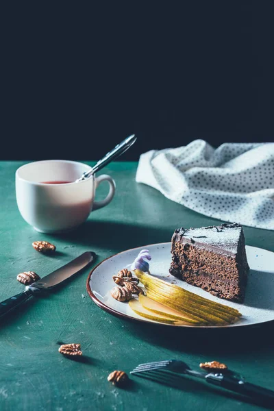 Close up view of piece of cake with cutted pear on plate and cup of tea on tabletop — Stock Photo