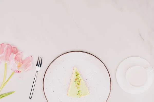 Vue du dessus du morceau de gâteau sur assiette, fleurs et tasse de lait sur surface blanche — Photo de stock