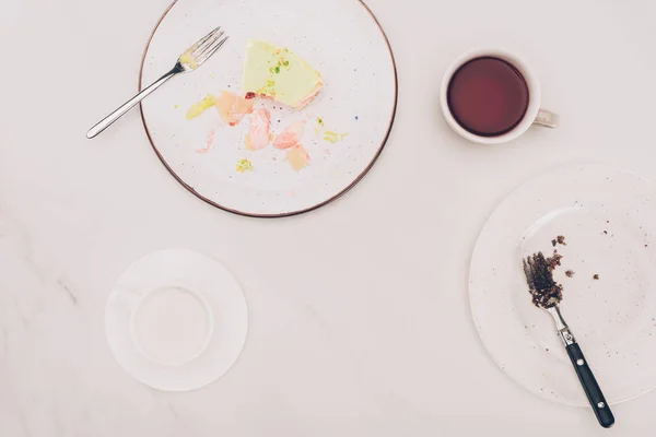 Draufsicht auf arrangierte Teller mit Kuchenstücken und Getränken auf weißer Tischplatte — Stockfoto