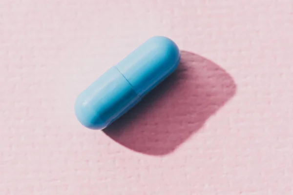 Vista de cerca de la medicina azul en la superficie rosa - foto de stock