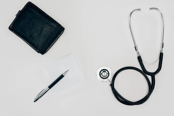 Draufsicht auf medizinisches Stethoskop, Geldbörse und Stift auf weißer Oberfläche — Stockfoto