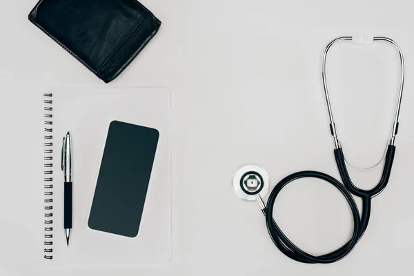 Top view of medical stethoscope, notebook and smartphone on white surface — Stock Photo