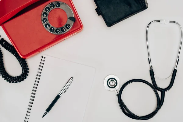 Draufsicht auf Telefon, Stethoskop, Notizbuch und Brieftasche auf weißer Oberfläche — Stockfoto